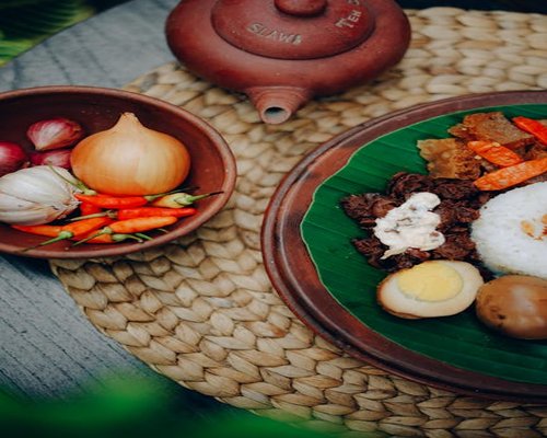 A traditional Indonesian meal with rice, tempeh, and fresh vegetables on a woven placemat